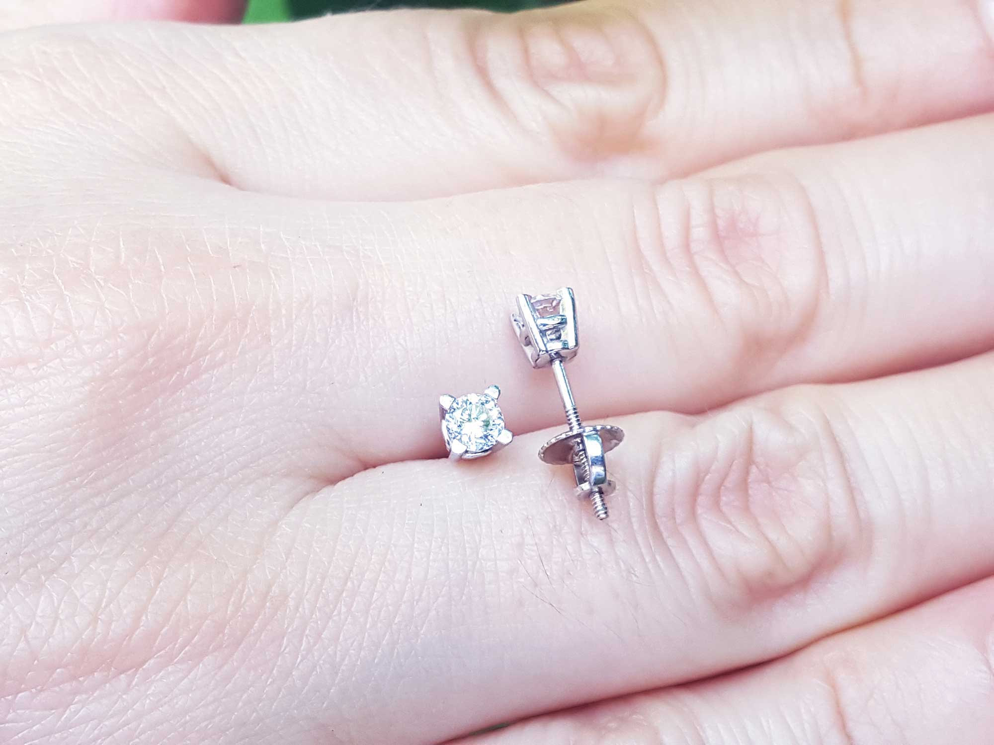 On a hand displaying a screw backs natural diamond stud earrings white gold.