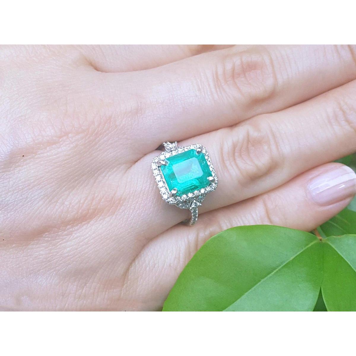 A green fire emerald ring on a hand with green leaves in the background.