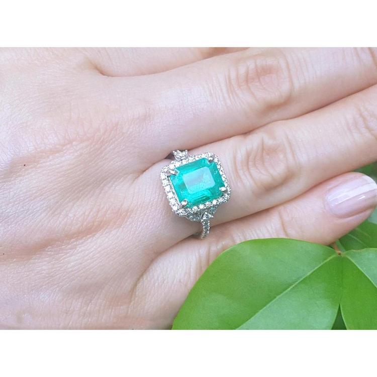Emerald-cut natural Colombian emerald ring with diamond halo, set in 14k white gold on a hand.