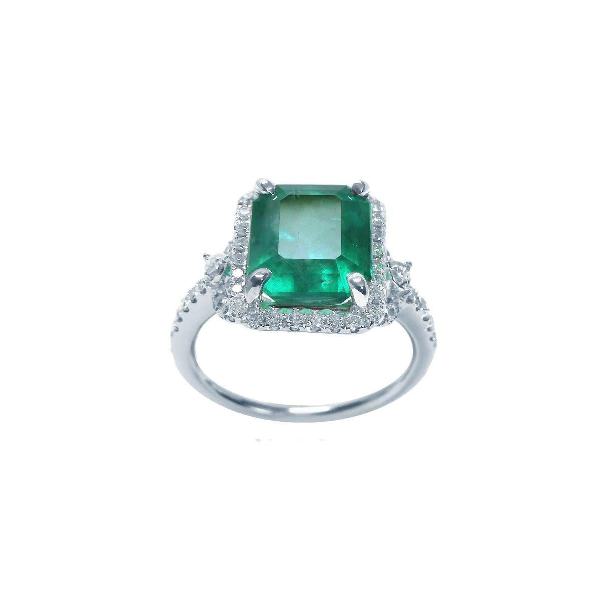 An emerald-cut emerald engagement ring with a halo diamond in white gold on a white background.