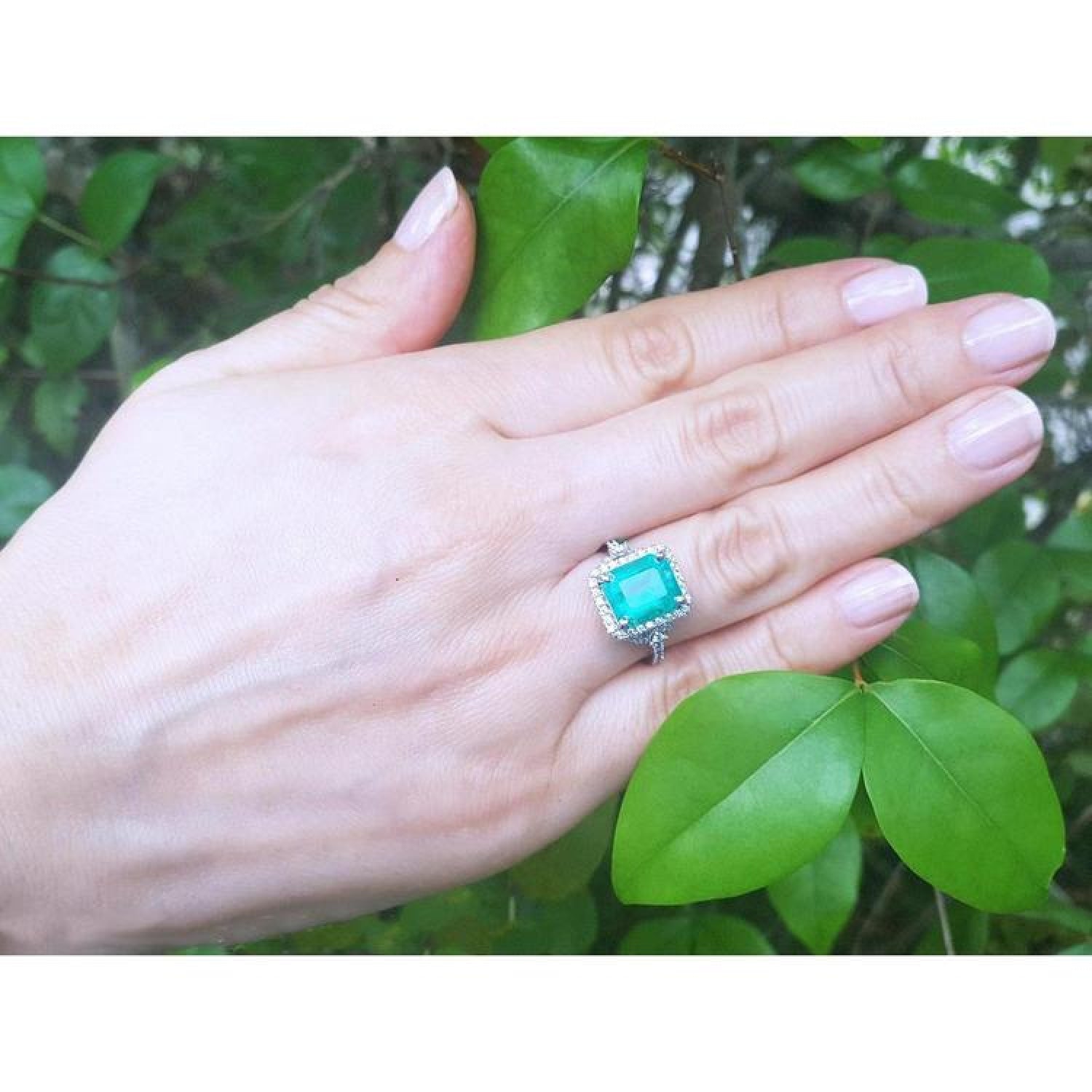 Emerald-cut natural Colombian emerald ring with diamond halo on a hand, 14k white gold.