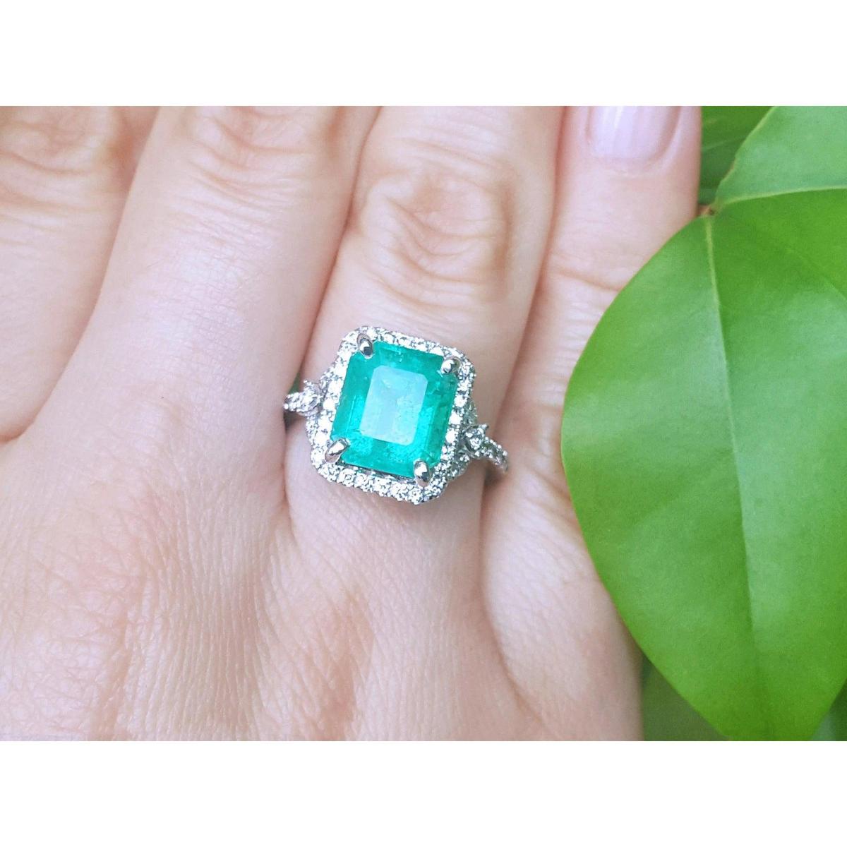 A brides' emerald engagement ring on a finger with a green leaf background.