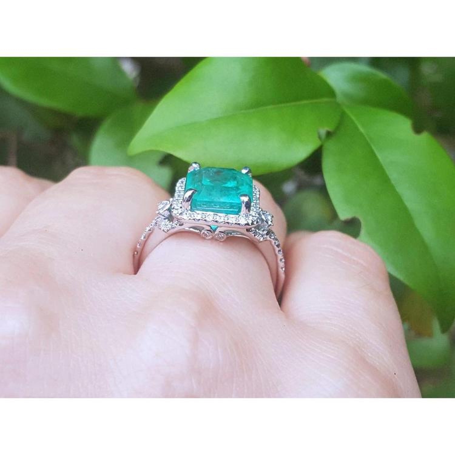 Emerald-cut natural Colombian emerald ring with diamond halo, set in 14k white gold, worn on a finger.