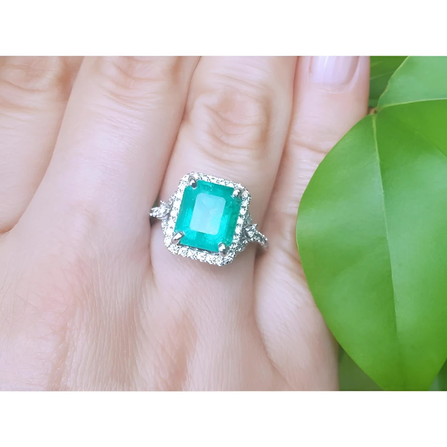 A natural colombian emerald ring for ladies with a halo diamond around the emerald is made of 14k white gold.