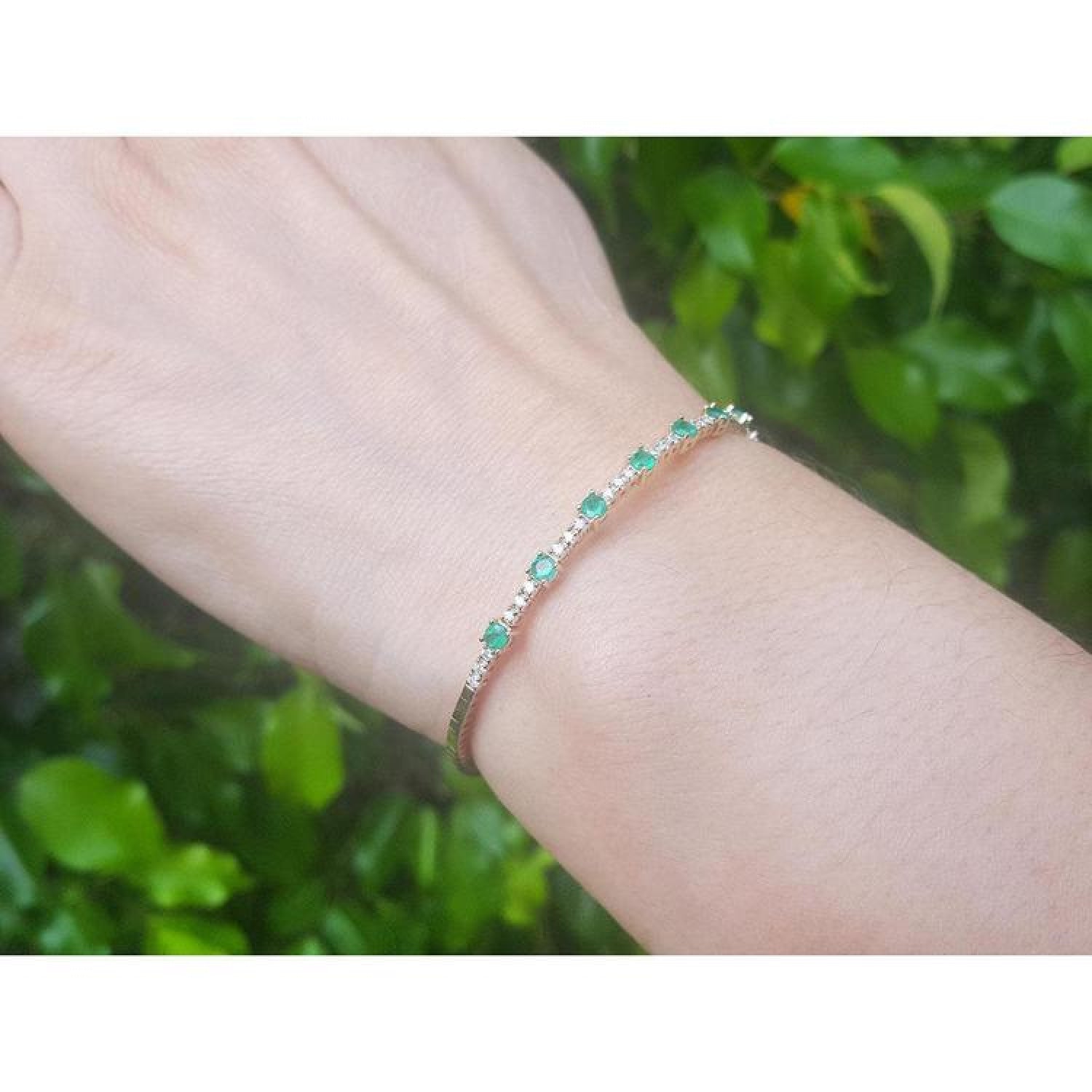 Flexible 14K yellow gold bangle bracelet with genuine Colombian emeralds and accent diamonds on a wrist.