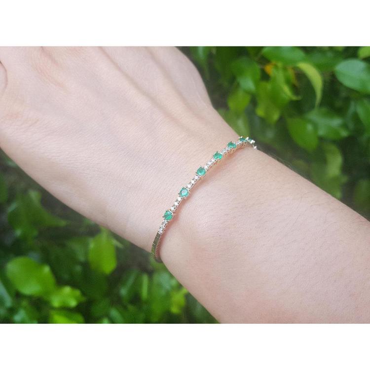 Flexible 14K yellow gold bangle bracelet with genuine Colombian emeralds and accent diamonds on a wrist.