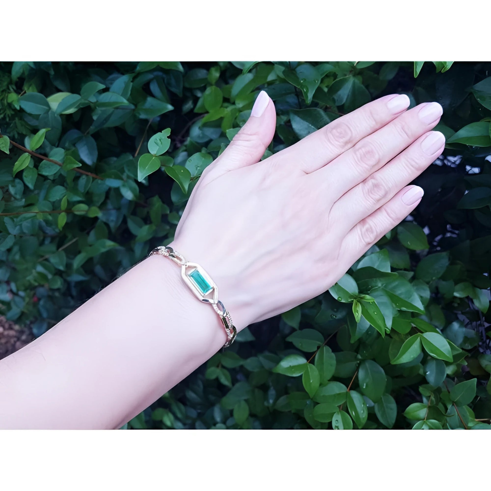 Woman's hand wearing a 14K yellow gold bracelet with a vibrant emerald-cut natural Colombian emerald.
