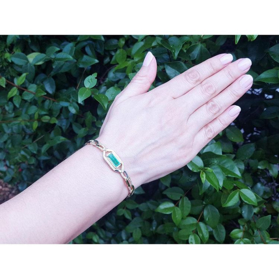 Woman's hand wearing a 14K yellow gold bracelet with a vibrant emerald-cut natural Colombian emerald.