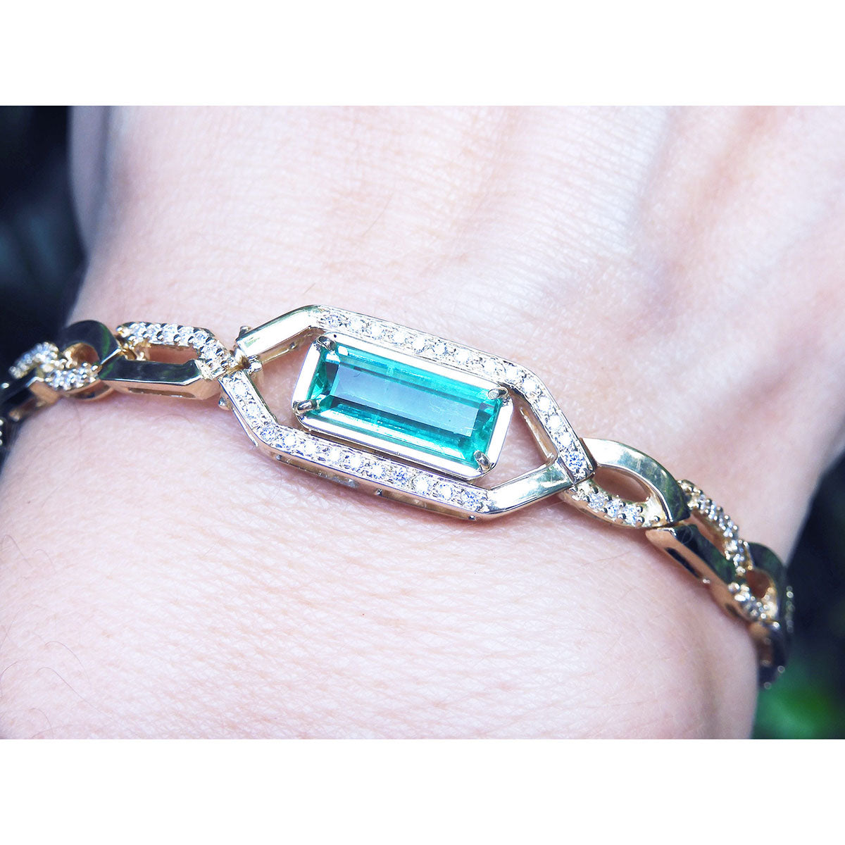 Gold bracelet with a rectangular natural colombian emerald and diamonds on a wrist.
