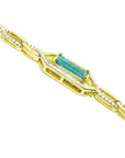 The side profile view of a gold bracelet with emerald and diamond accents on a white background