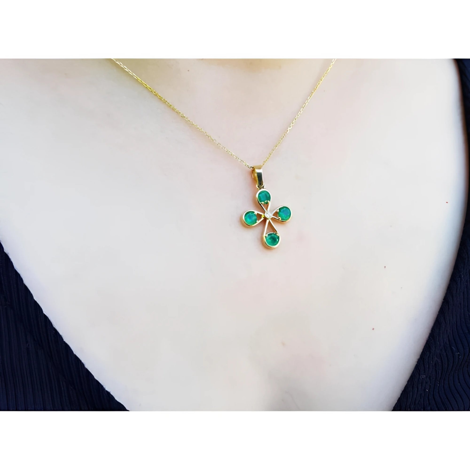 18K yellow gold cross pendant with four round Colombian emeralds and a small diamond, worn on a gold chain.
