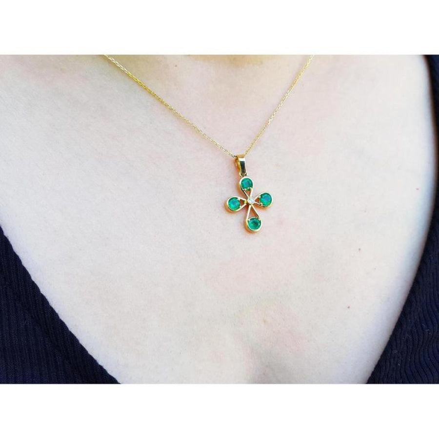 18K yellow gold cross pendant with four round Colombian emeralds and a small diamond, worn on a gold chain.