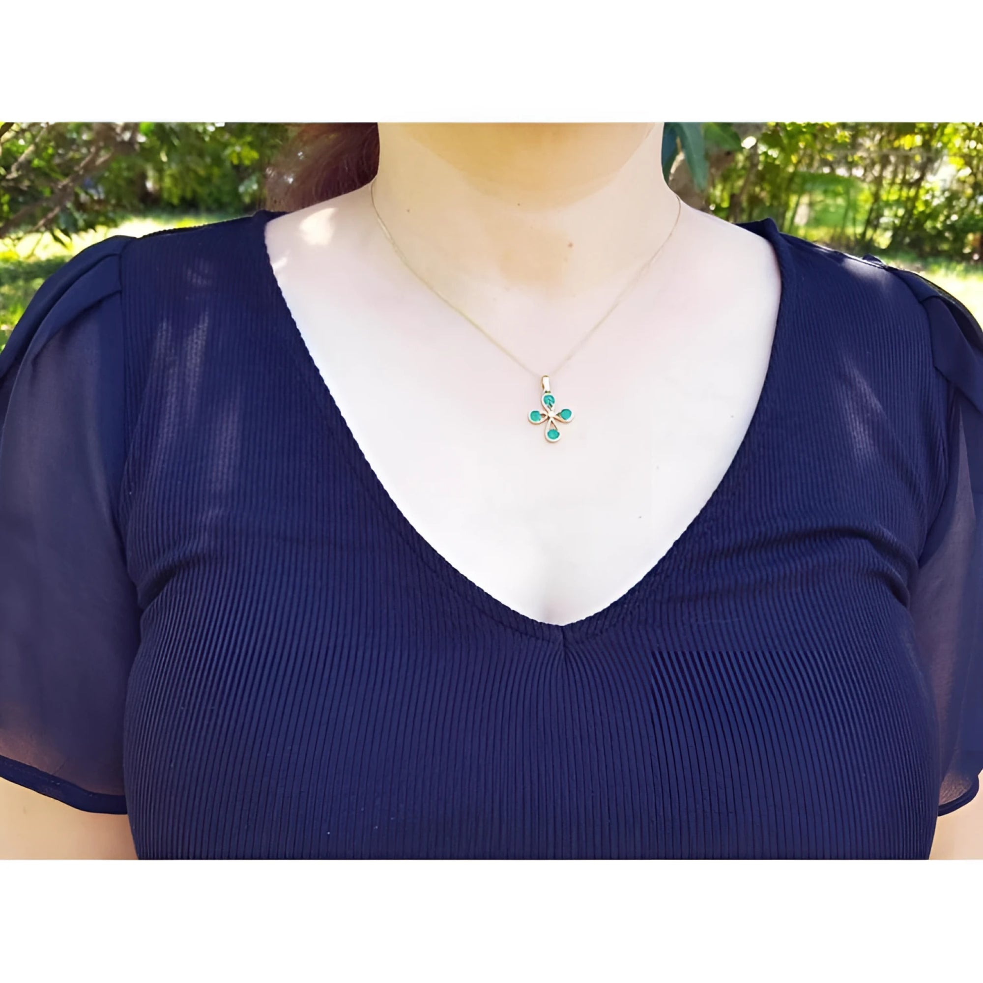 18K yellow gold cross pendant with four round natural Colombian emeralds, worn on a woman's neck.