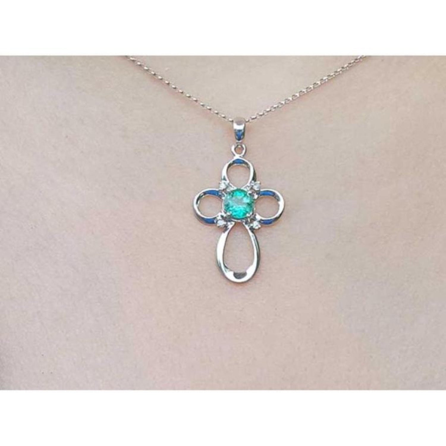 14K white gold cross pendant with a round Colombian emerald and diamond accents on a chain.