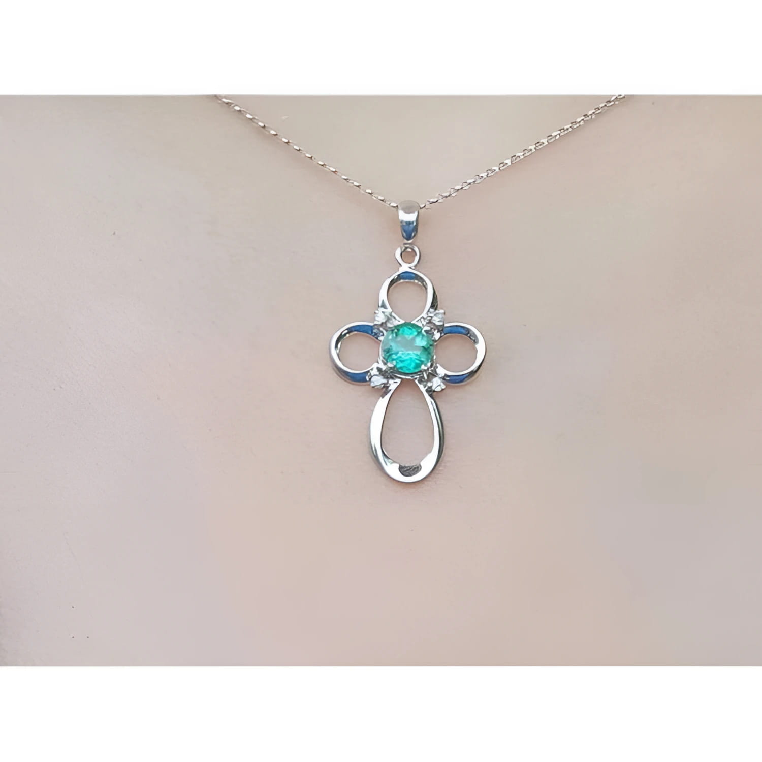14K white gold cross pendant with a round Colombian emerald and diamond accents on a chain.