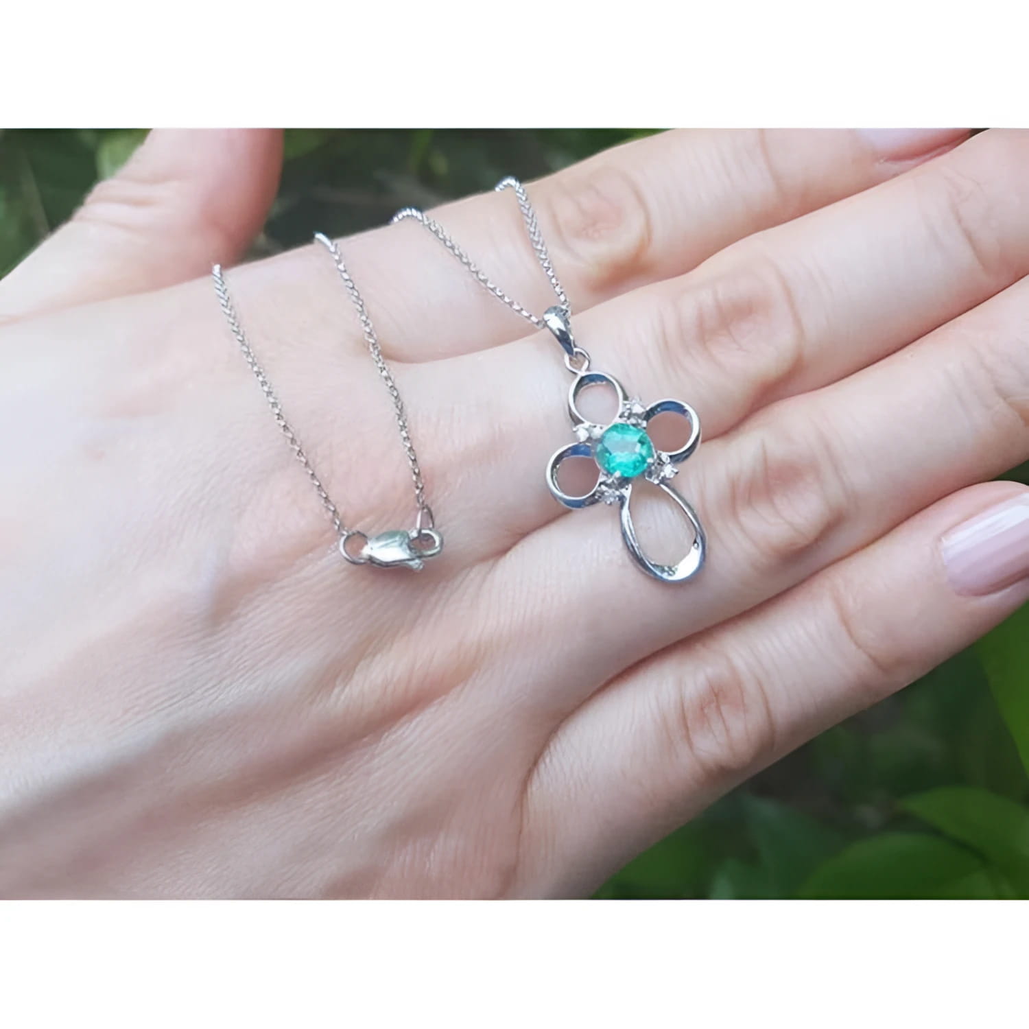 14K white gold cross pendant with a round-cut Colombian emerald and diamond accents, on a delicate chain.