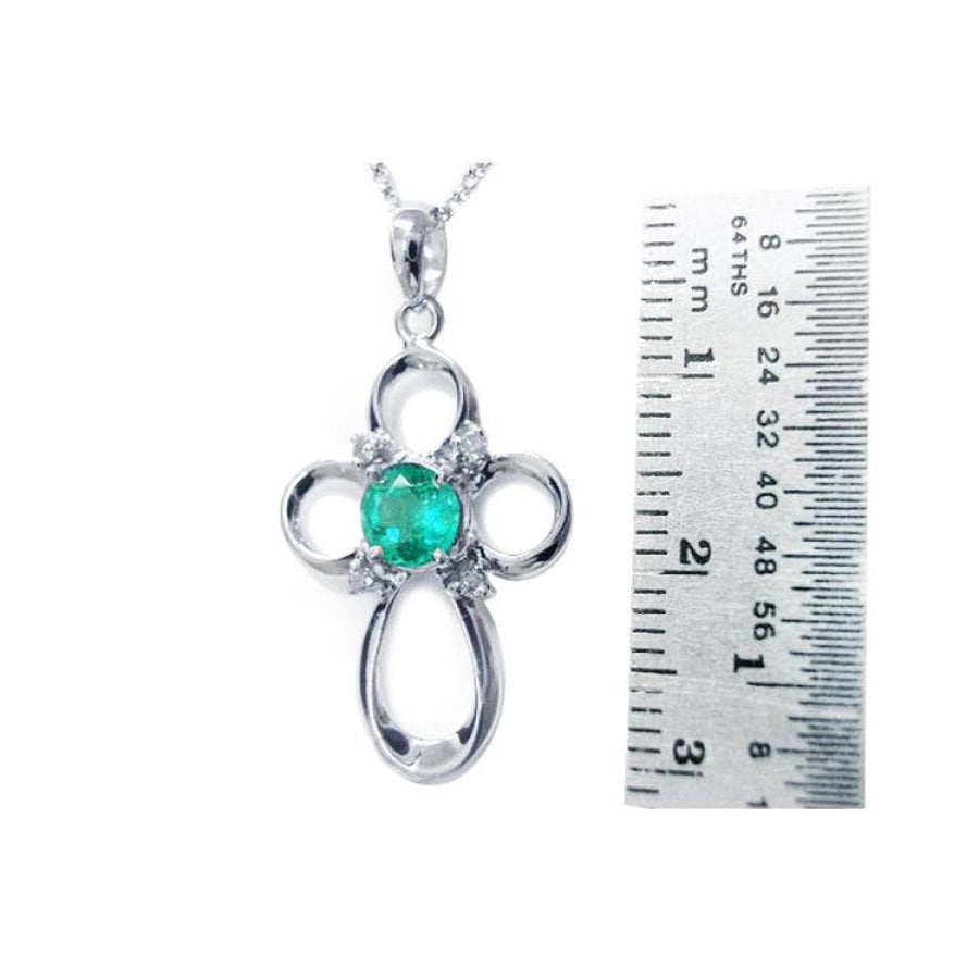 14K white gold cross pendant with a round green Colombian emerald and diamond accents, next to a ruler.