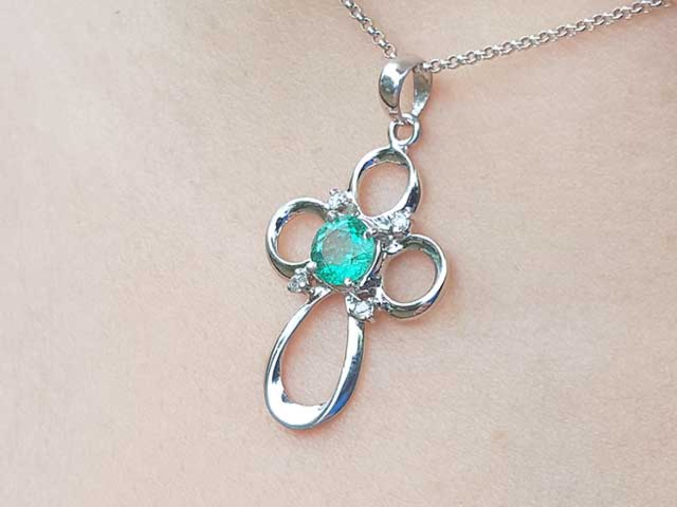 A white gold emerald pendant on a chain, worn on a person's neck.
