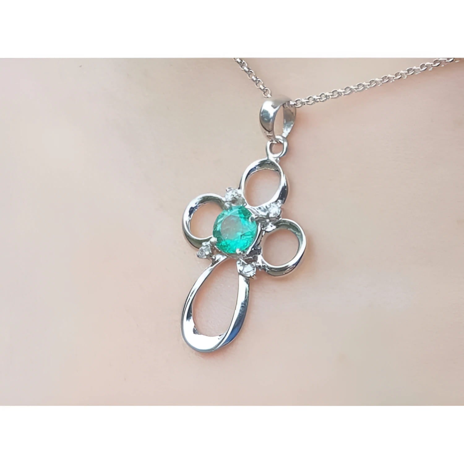 A white gold emerald pendant on a chain, worn on a person's neck.