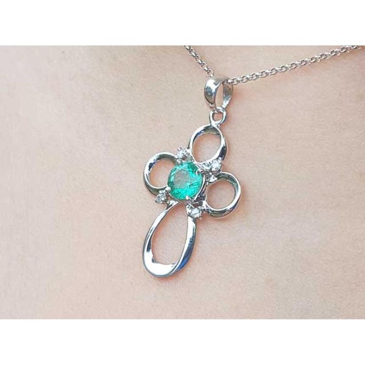 A white gold emerald pendant on a chain, worn on a person's neck.