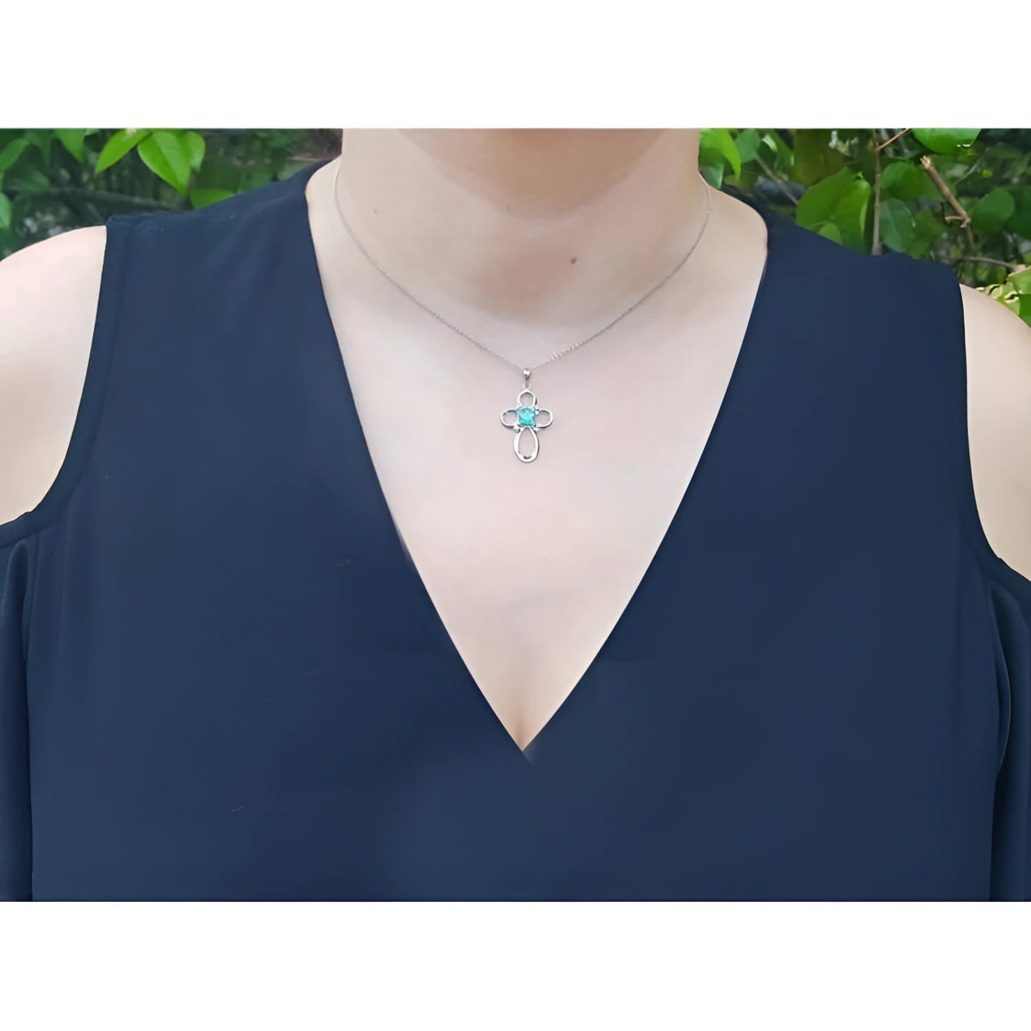 14K white gold cross pendant with a 0.57 ct round Colombian emerald and diamond accents, worn on a necklace.
