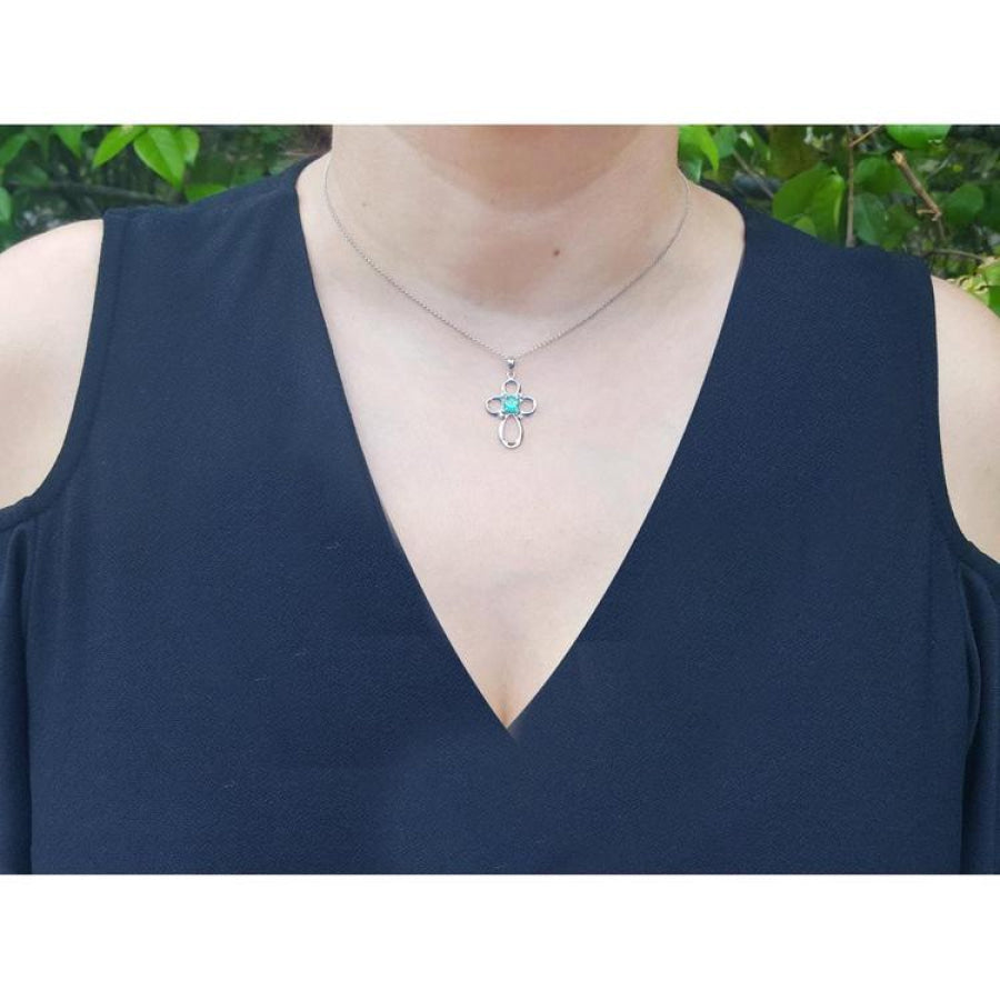 14K white gold cross pendant with a 0.57 ct round Colombian emerald and diamond accents, worn on a necklace.