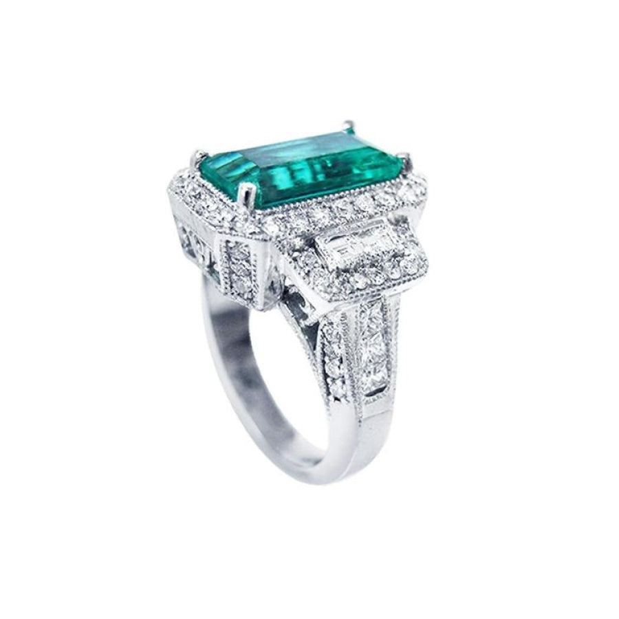 18K white gold ring with a vibrant emerald-cut Colombian emerald, haloed by diamonds and baguette side stones.