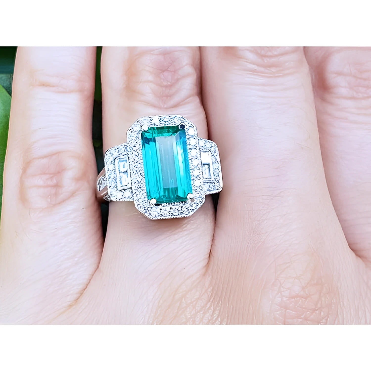 A GIA certified genuine Colombian emerald ring rectangular emerald-cut surrounded by natural diamonds in 18k white gold on a finger.