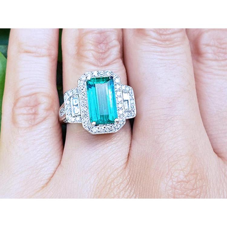 A GIA certified genuine Colombian emerald ring rectangular emerald-cut surrounded by natural diamonds in 18k white gold on a finger.