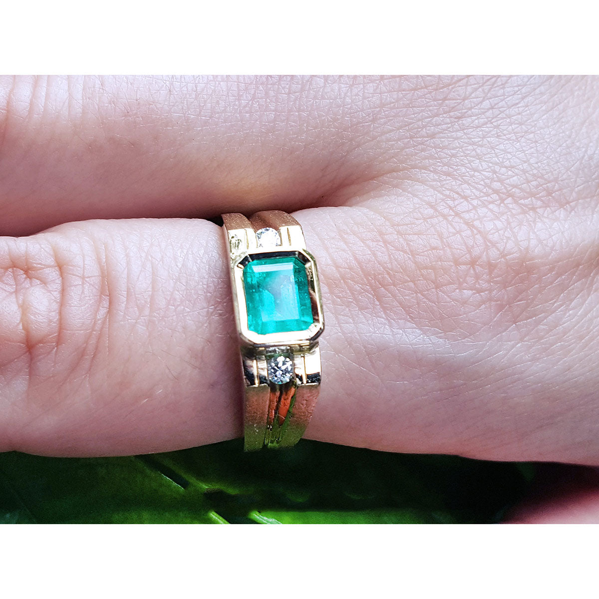 Gold mens ring with a natural emerald bezel set on a finger.