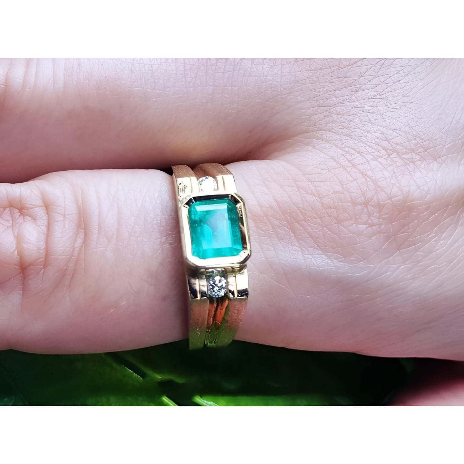Men's 14K yellow gold ring with a bezel-set emerald and side diamond accents on a finger.