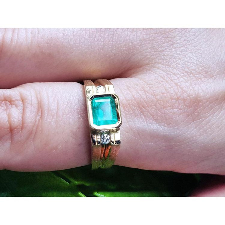 Men's 14K yellow gold ring with a bezel-set emerald and side diamond accents on a finger.