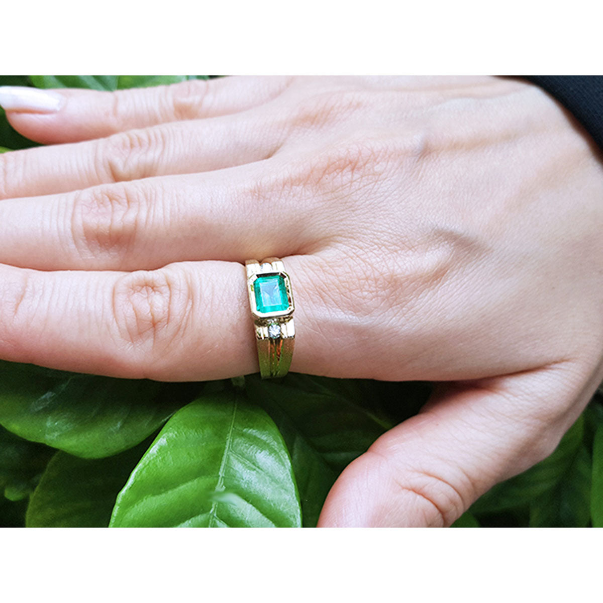 A yellow gold men&#39;s emerald ring on a hand against a leafy background.