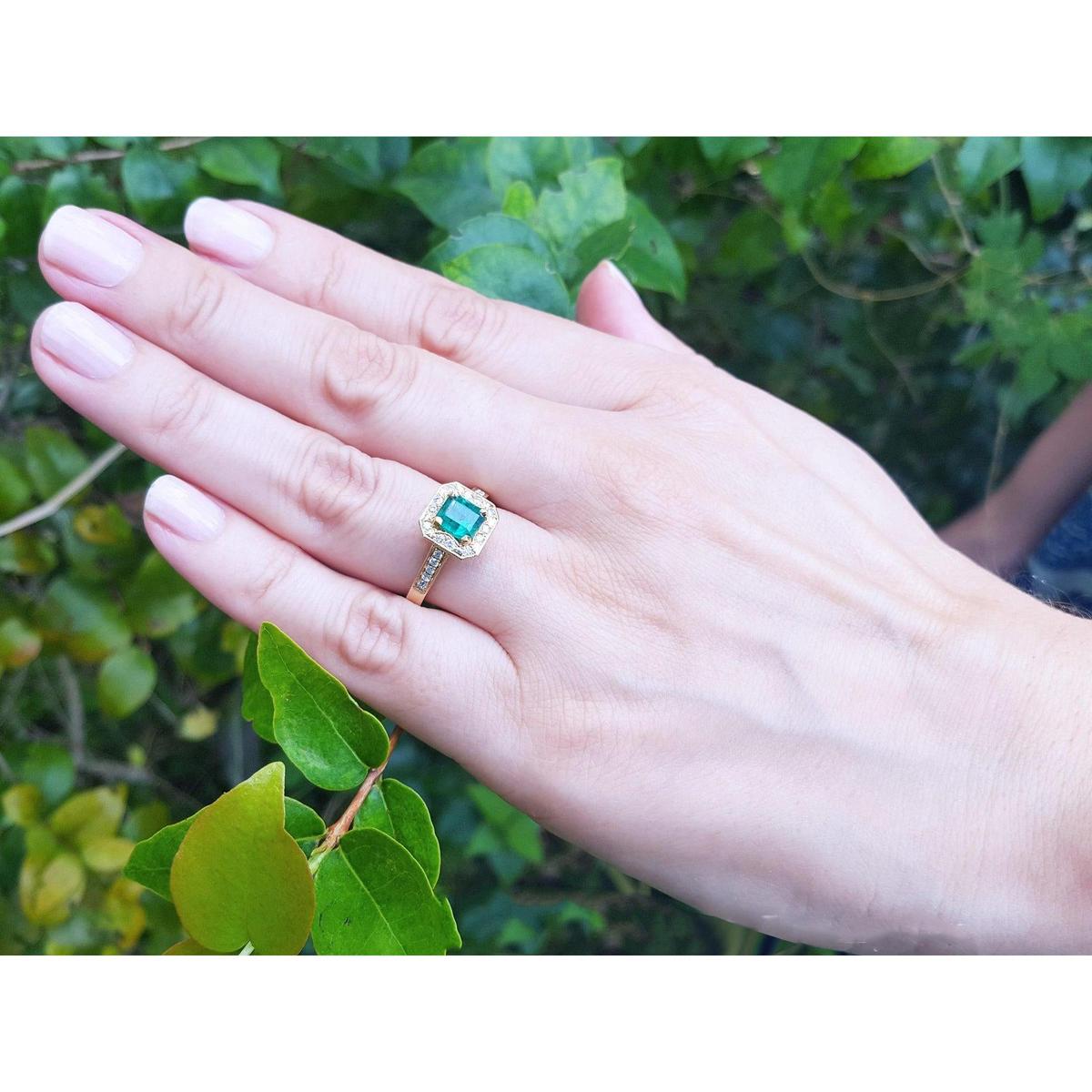 Hand wearing a Mother's Day gift emerald ring against a green leafy background.
