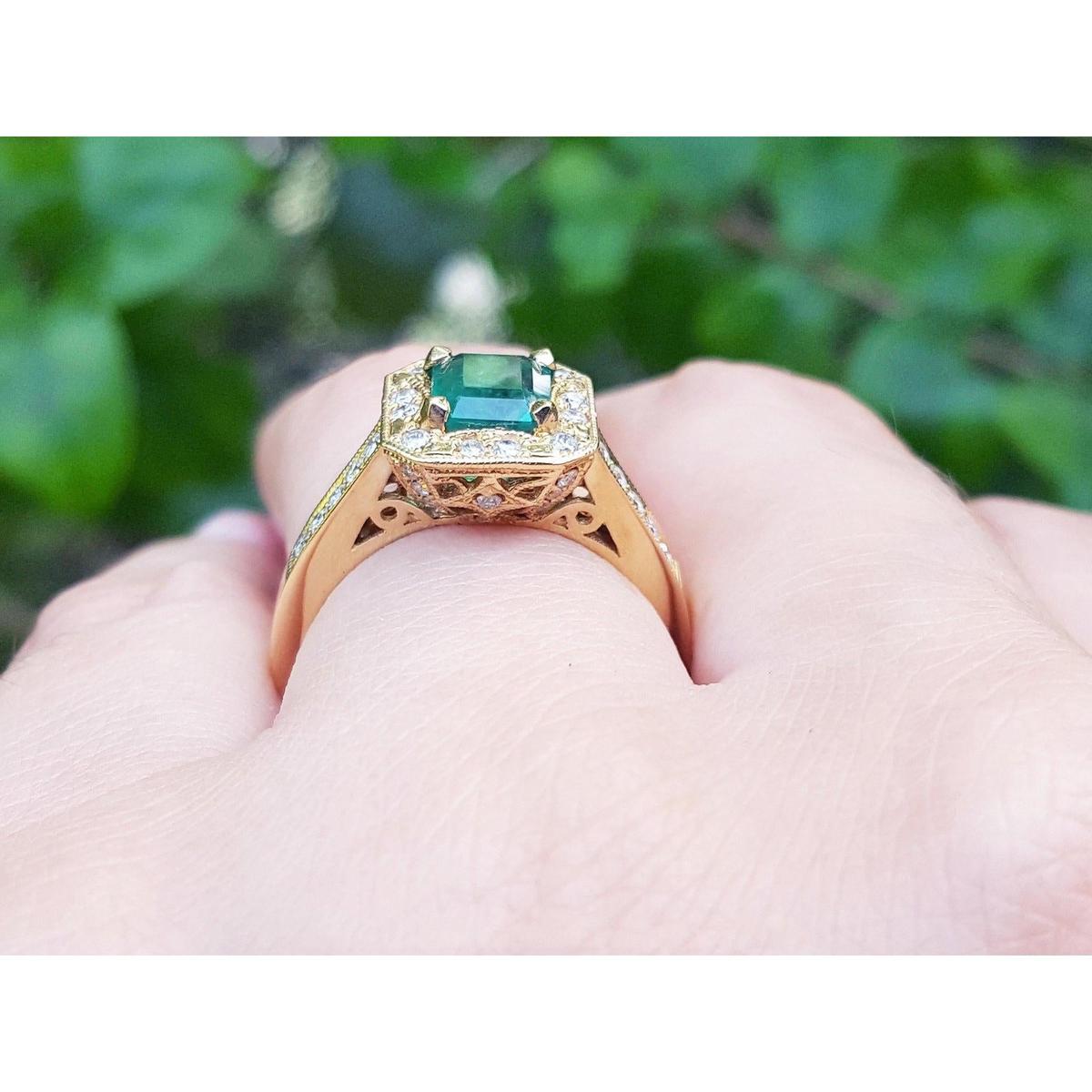 Gold ring with a natural emerald on a hand against a blurred green background.