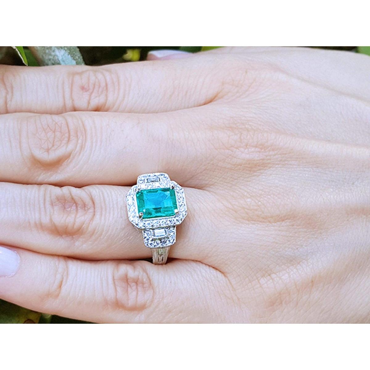 Emerald engagement ring with diamond accents on a hand.
