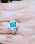 Emerald engagement ring with diamond accents on a hand.