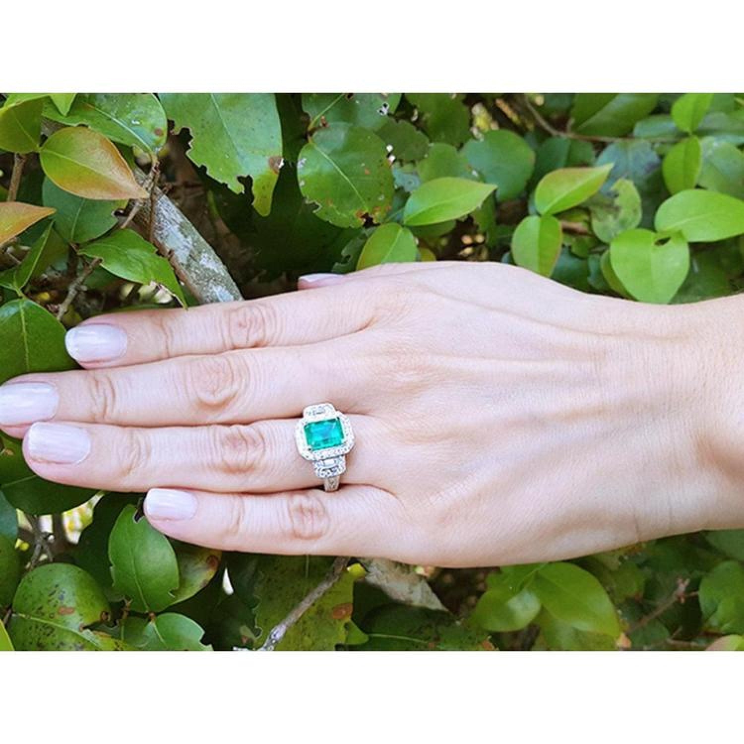 Hand wearing an 18K white gold engagement ring with a vibrant emerald and diamond halo.