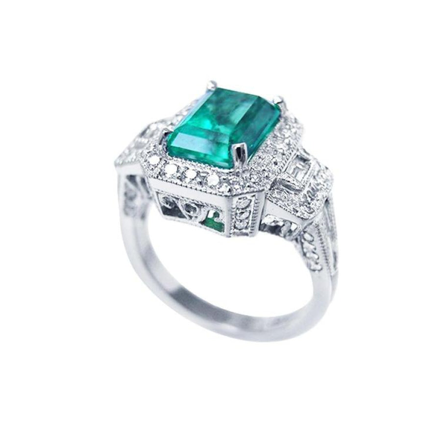 Vibrant 2.47 ct. emerald engagement ring in 18K white gold with diamond halo and baguette side diamonds.