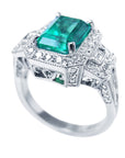 An elegant natural emerald engagement ring and diamond accents on a white background.