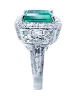 A side profile of a natural emerald and a halo diamond engagement ring in 18k white gold.