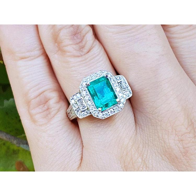 A natural emerald ring with a halo diamond accent on a finger is made of 18k white gold.
