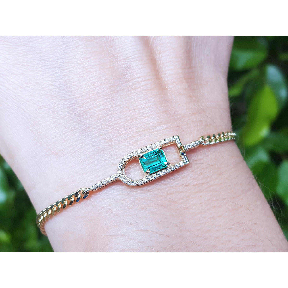 A natural emerald-cut women's emerald bracelet handcrafted in 14k yellow gold on a wrist.