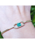 A natural emerald-cut women's emerald bracelet handcrafted in 14k yellow gold on a wrist.