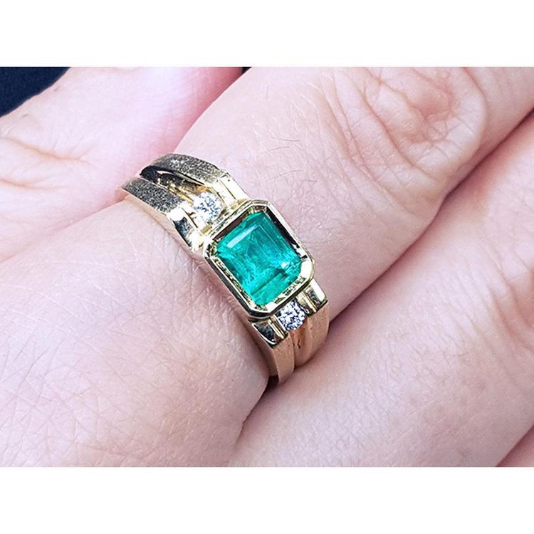 A 14k yellow gold men's ring with a bezel set emerald on a person's finger.