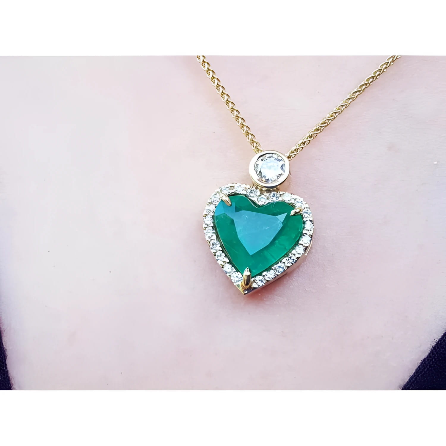 Heart-shaped emerald pendant with diamond halo and round diamond accent on an 18k gold chain.