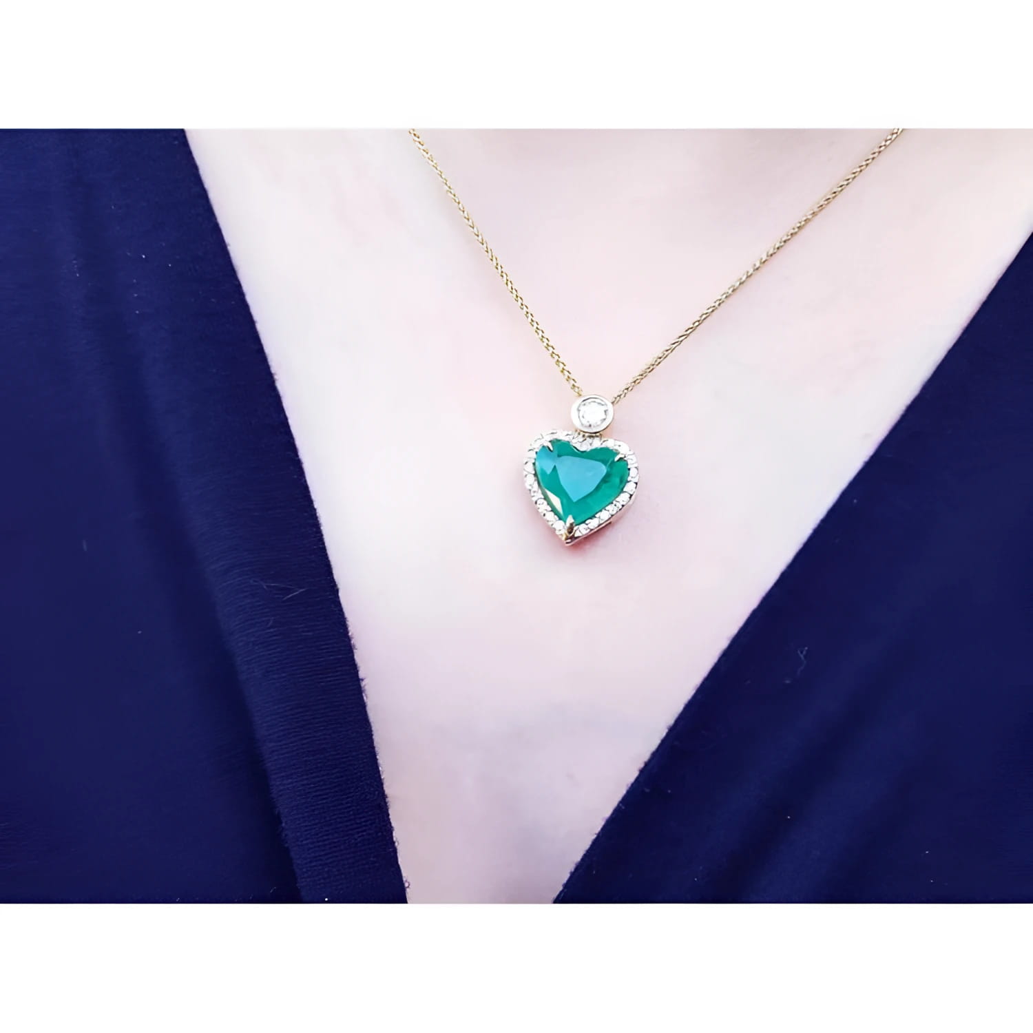 Emerald heart pendant with diamond halo on an 18k gold chain, worn on a dark top.