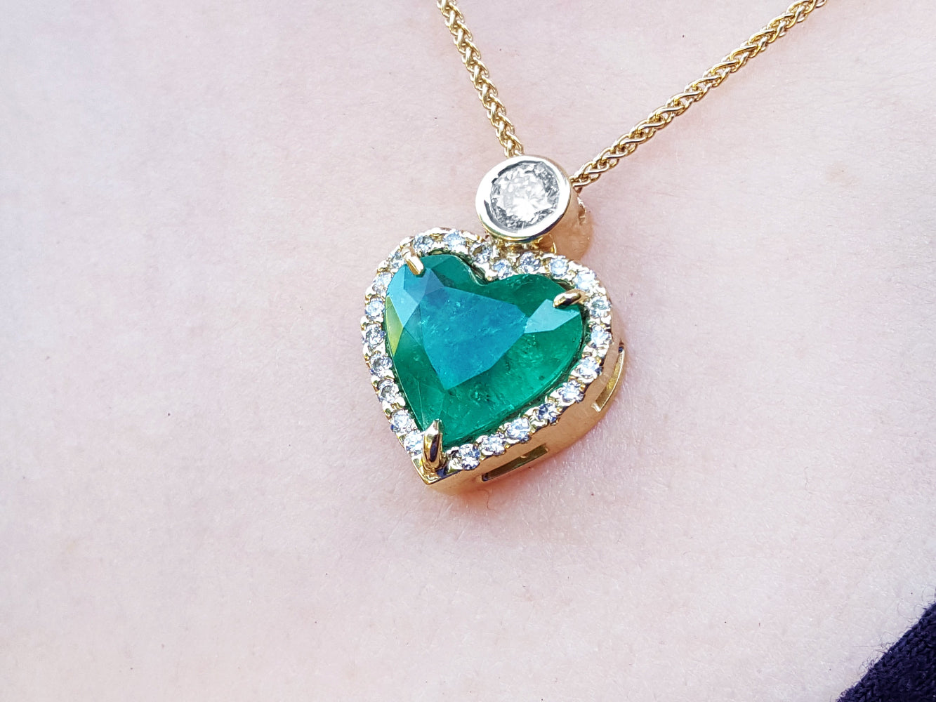 Heart-shaped emerald pendant with gold chain on a light pink background