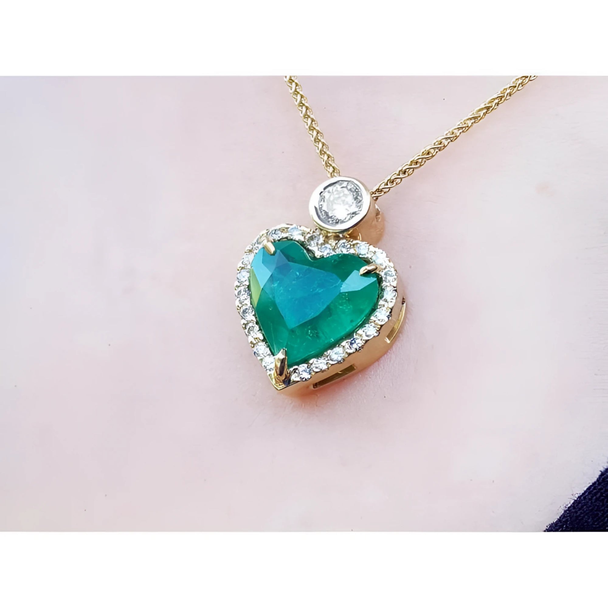 Heart-shaped emerald pendant with gold chain on a light pink background