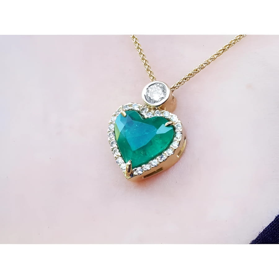 Heart-shaped emerald pendant with gold chain on a light pink background